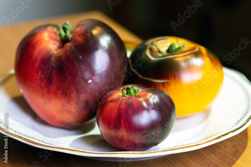 Yellow-black and pink-black tomatoes on a white plate, close-up