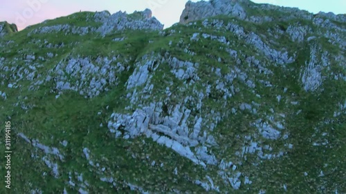 FPV drone shot panning over the Schaefler Ridge, revealing a hiker on a mountain peak, at sunset, on a sunny summer evening, in Appenzell Alps, Switzerland photo