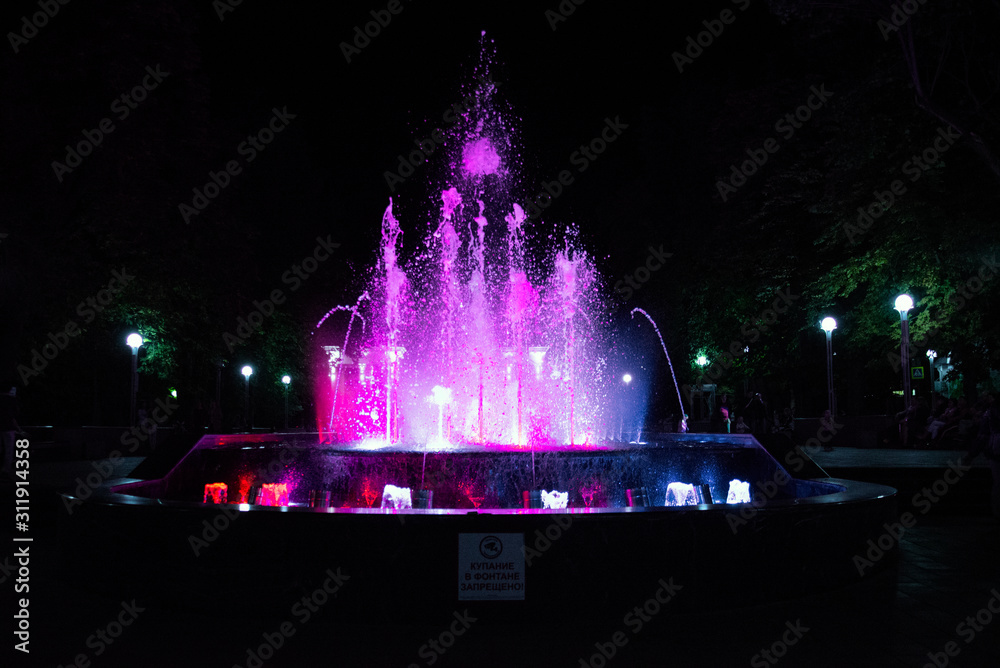Drops scatter in the fountain with pink backlighting at night, close-up. Translation of the caption in the ad: 