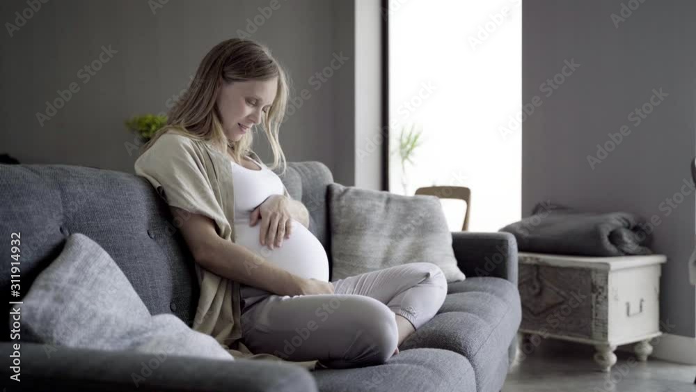 Beautiful pregnant woman sitting on sofa and talking with baby. Happy future mother touching tummy at home. Pregnancy concept Beautiful pregnant woman sitting on sofa and talking with baby. Happy future mother touching tummy at home. Pregnancy concept