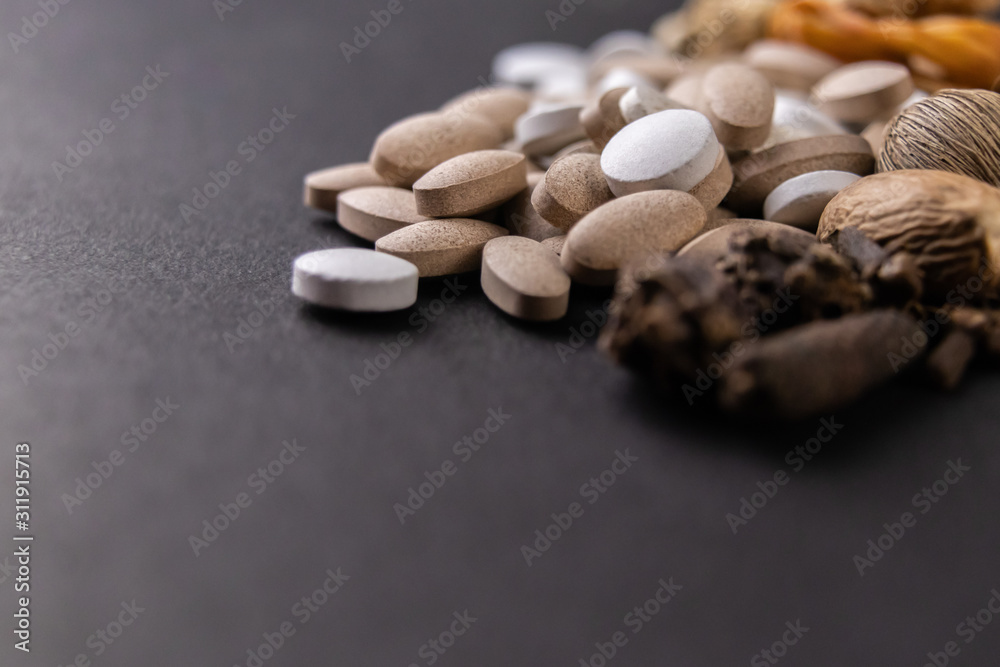 Herbal medicine concept. macro shot of white and brown tablets with dried herbs on a black background with copy space Herbal medicine concept. macro shot of white and brown tablets with dried herbs on a black background with copy space