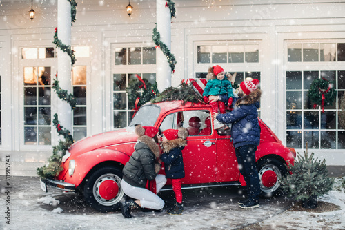 Parents and children with New Year presents and Christmas tree. Dad, mom, daughters and son are going for Christmas holidays by car