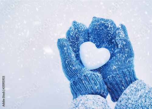 Female hands in knitted mittens with heart of snow in winter day. Love concept. Valentine day background. photo