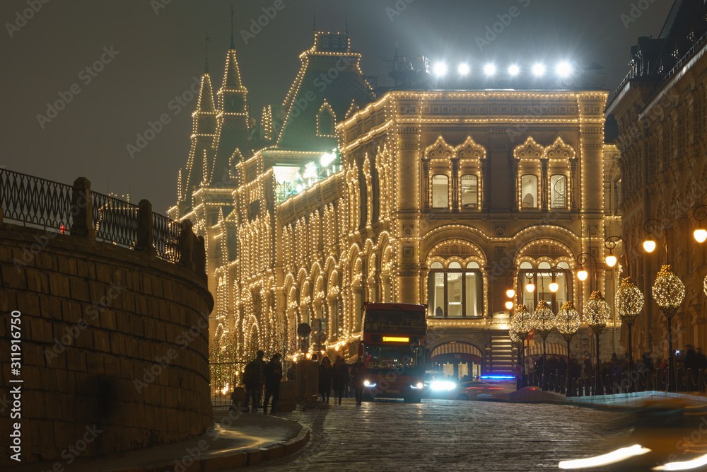Bright illuminated facade of the GUM (Central Department store) in Moscow. Lighting of the Red Square during winter night. Silhouettes of touristic bus and people. Holidays and festive mood concepts. 