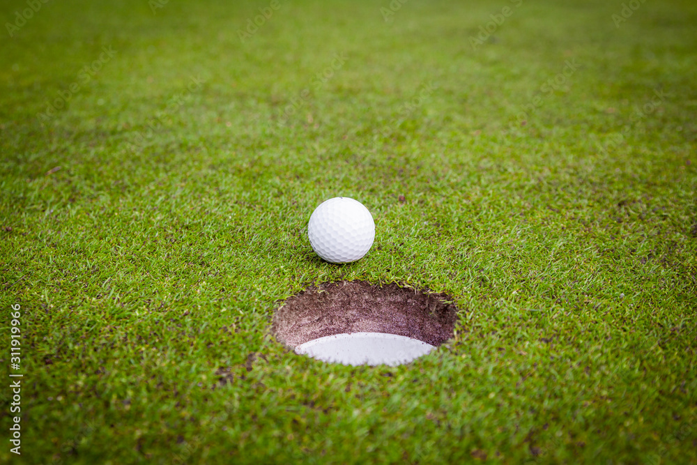 Golf ball on green meadow. golf ball on lip of cup