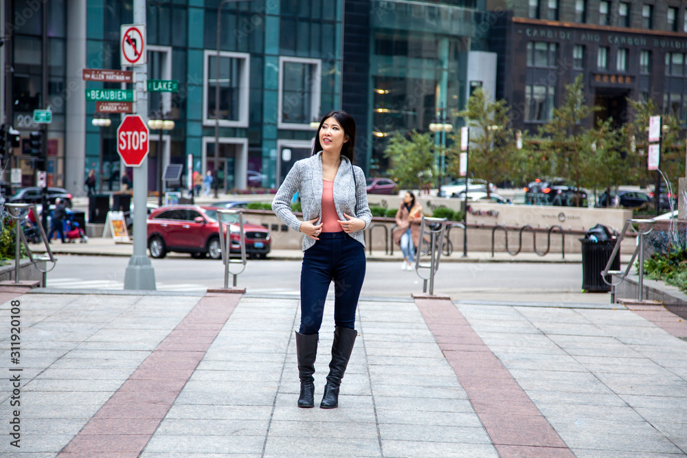 Obraz premium Chicago,IL/USA- November 10th 2019:a happy Asian business woman with long black hair wearing a comfortable trendy fall sweater is walking confidently carrying a fashionable handbag in downtown area