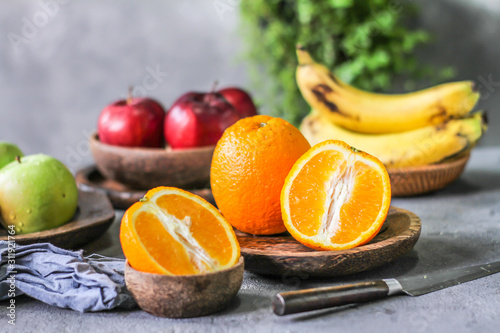 Photo of fresh orange on retro background. Slice of orange in front of fruits and vegetables. Half of the orange on wooden plate bowl. Sunkist. Summer. Image