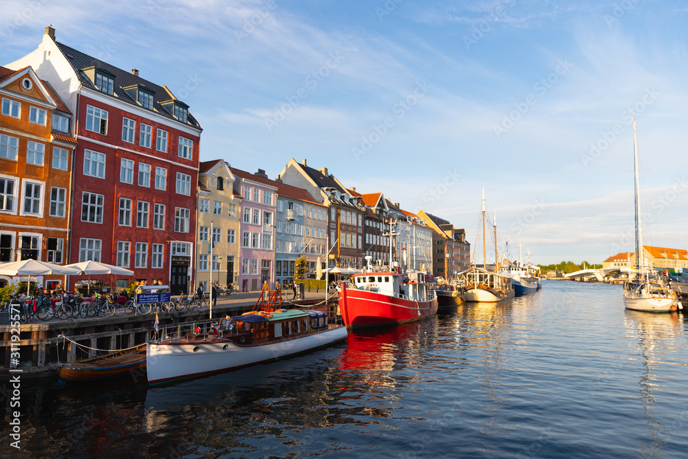 Colorful houses and boats in the canals of Nyhavn district, Copenhagen, Denmark on sunny evening