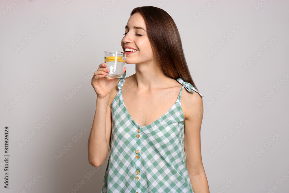 Young woman drinking lemon water on light background Young woman drinking lemon water on light background