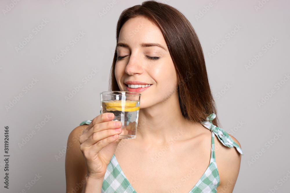 Young woman drinking lemon water on light background Young woman drinking lemon water on light background
