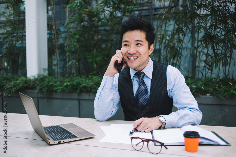 Cheerful modern Asian businessman speaking on phone on terrace Cheerful modern Asian businessman speaking on phone on terrace