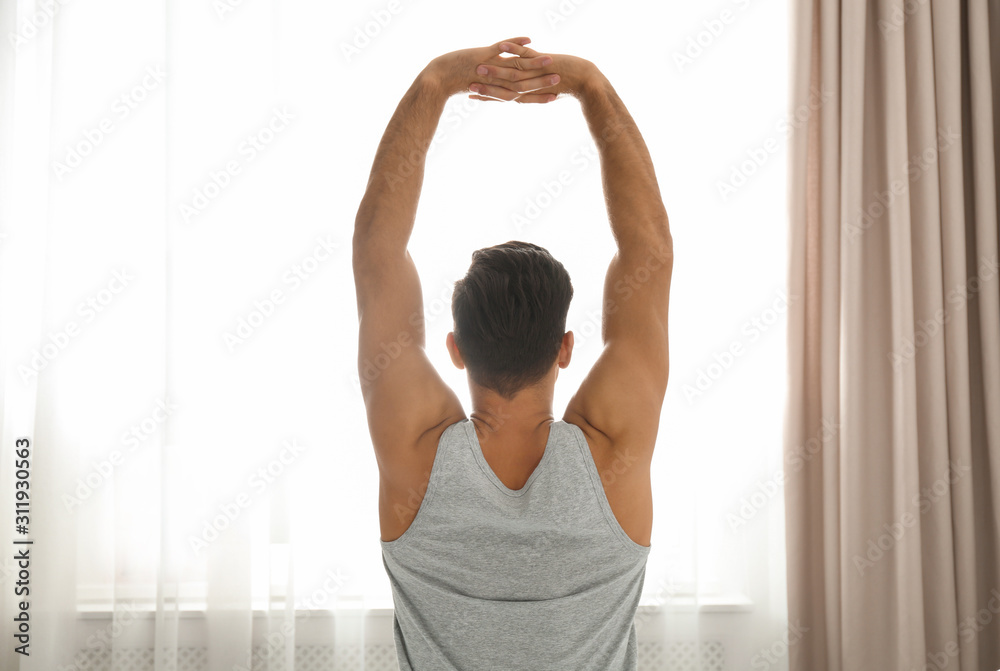 Fototapeta premium Man stretching near window at home. Lazy morning