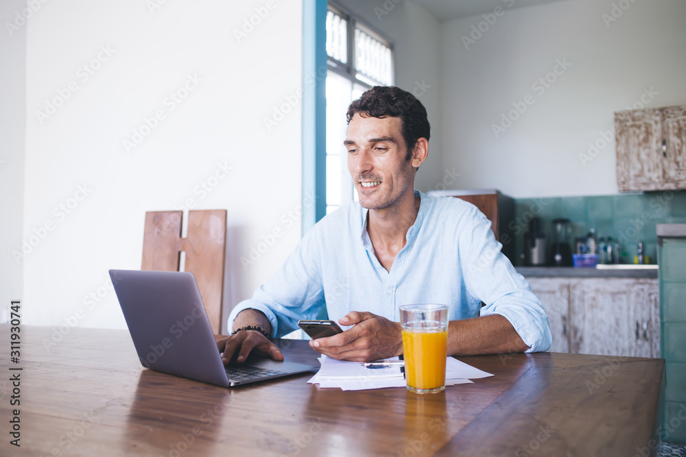 Adult man with smartphone using laptop at home Adult man with smartphone using laptop at home
