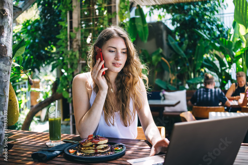 Modern young freelancer talking on phone during work in cafe