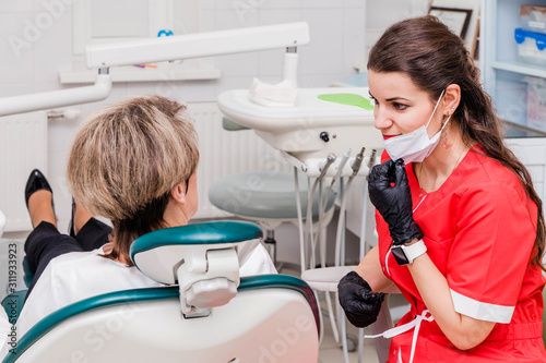 Young woman dentist in a red suit examines a patient