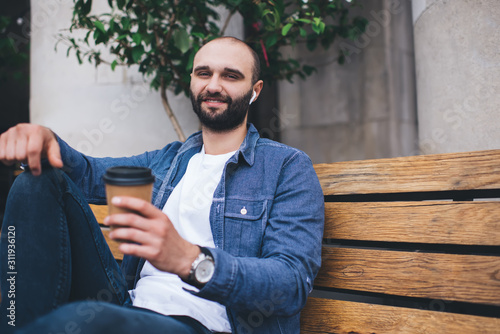 Smiling man with takeaway coffee taking rest on bench