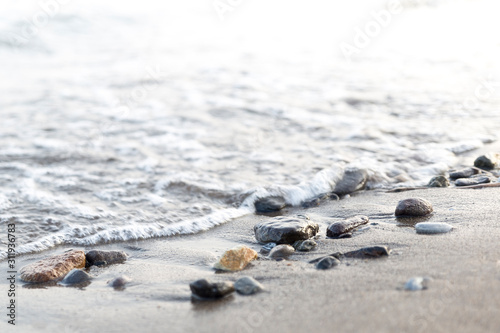 Wet pebbles on seashore in sun light. Sea wave on seacoast with round stones. 