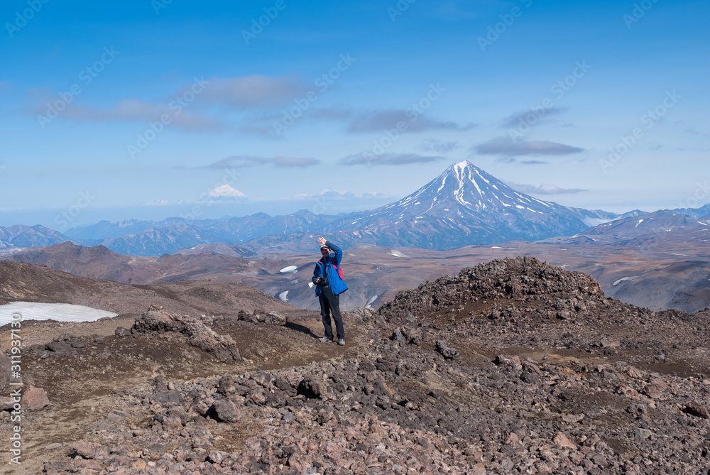 young man traveler photographer at the top of the volcano mountain shows excellent, rejoices, volcanic view in the crater of the volcano, the traveler at the height, the view of the mountain tops