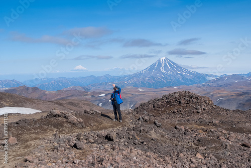 young man traveler photographer at the top of the volcano mountain shows excellent, rejoices, volcanic view in the crater of the volcano, the traveler at the height, the view of the mountain tops