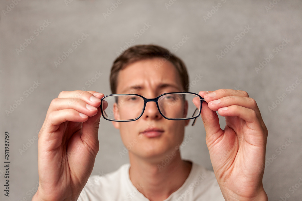 the young man holds glasses with diopter lenses and looks through them, the problem of myopia, vision correction