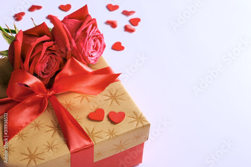 Fototapeta Naklejka Na Ścianę i Meble -  Golden gift box with red ribbon, roses and little hearts, concept of Valentine's day, anniversary, mother's day or birthday greeting, copy space, closeup view.
