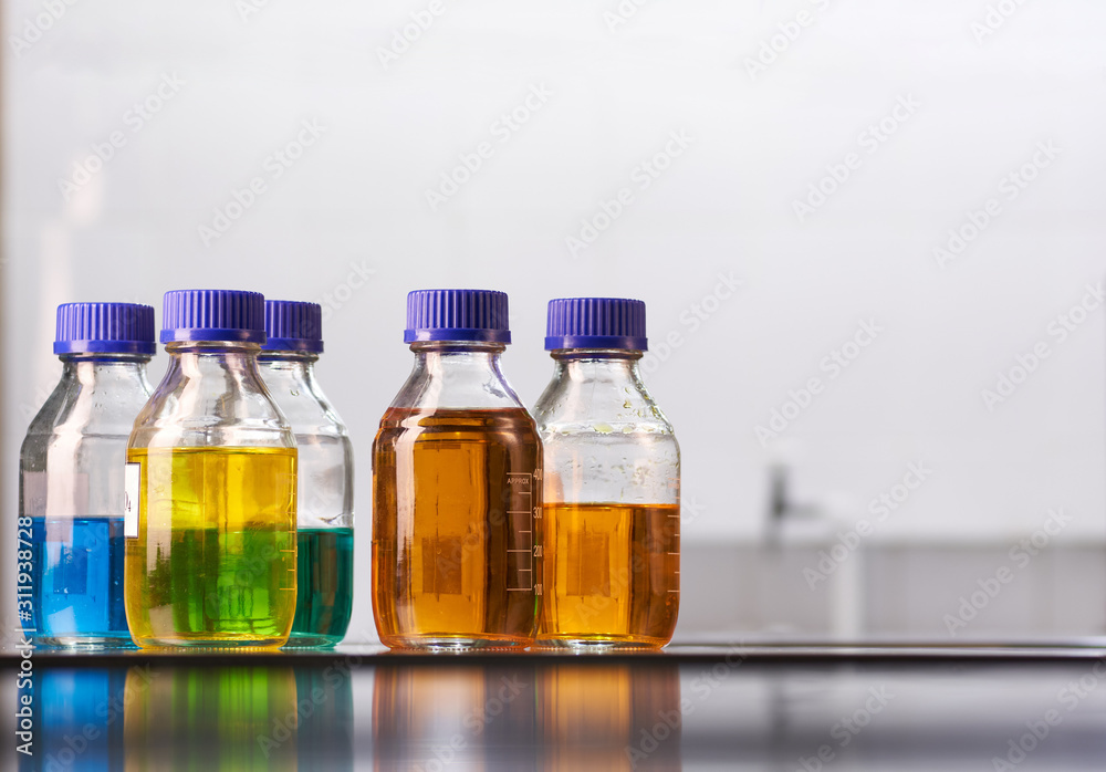 A set of jars with multicolored reagent solutions in a real laboratory. Large light empty space for text placement. A set of jars with multicolored reagent solutions in a real laboratory. Large light empty space for text placement.