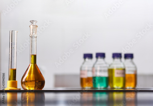 A set of jars and flasks with colored reagent solutions in a real laboratory. Large light empty space for text placement.