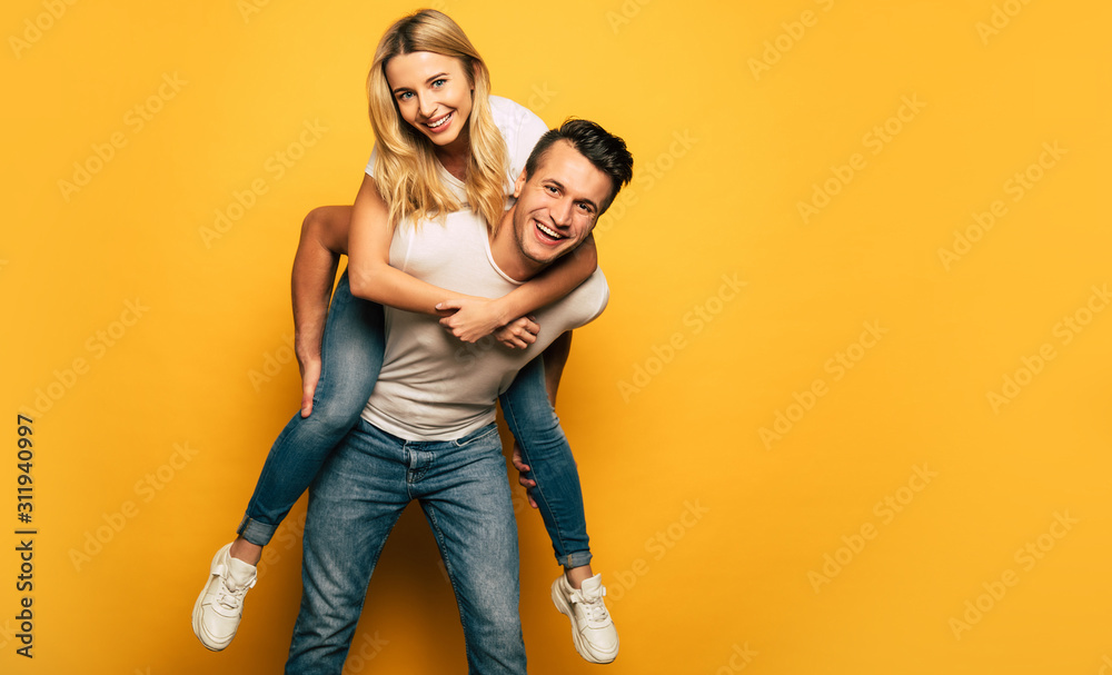 Playing around. Full-length photo of a happy man, giving his smiley girlfriend a piggyback ride while laughing out of joy. - obrazy, fototapety, plakaty 