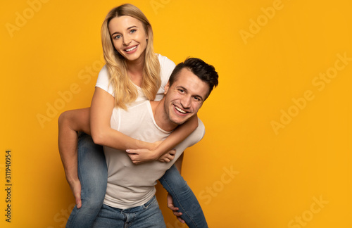 Having fun together. A handsome man is giving his blonde girlfriend a piggyback ride while laughing out of joy.