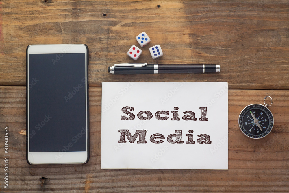 Social Media Words written on white on wooden desk with dice,compass,smart phone and pen.Top view conceptual