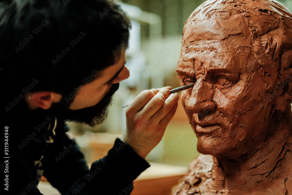 Focused sculptor finishing a clay head - obrazy, fototapety, plakaty 