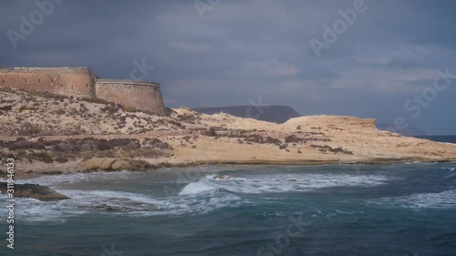 Castle San Ramon above beach of El Playazo, Cabo de Gata, province AlmerĂ­a, Andalusia Spain. Rocky sea shore with waves splashing in slow motion. Tourist site photo