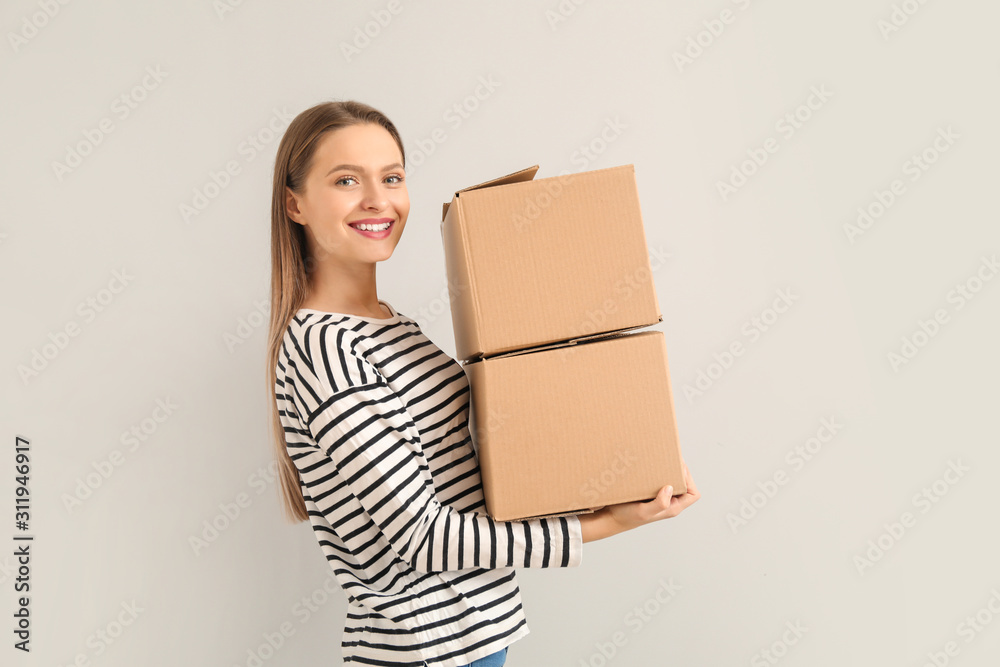 Happy young woman with moving boxes on light background Happy young woman with moving boxes on light background