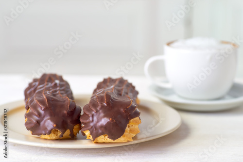 Two eclairs and cup of cappuccino on white wooden table