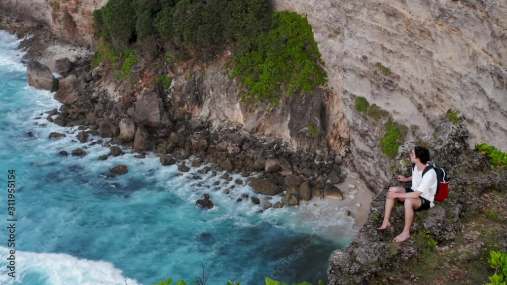 Guy sits on edge of cliff. Young boy coming to edge of cliff and sitting down. Man sitting and looking at horizon. Boy comes to edge of crag and sits on rock. Lonely guy sitting over cliff Guy sits on edge of cliff. Young boy coming to edge of cliff and sitting down. Man sitting and looking at horizon. Boy comes to edge of crag and sits on rock. Lonely guy sitting over cliff