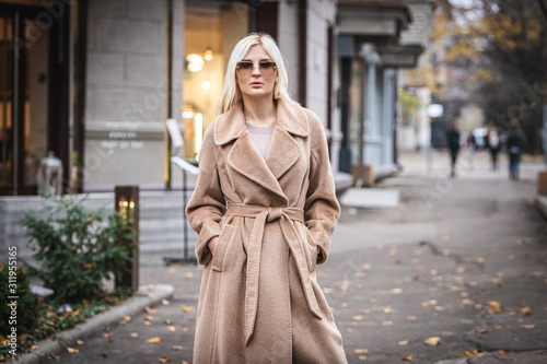 Young beautiful blond woman in an autumn coat stands on a city street. Soft focus. Fashionable concept.