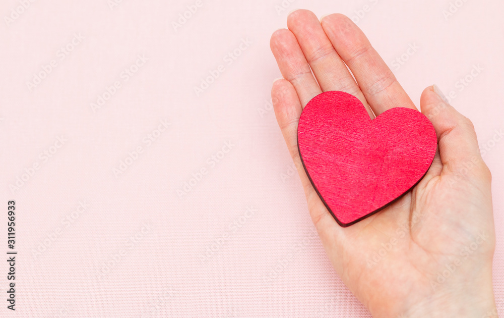 Obraz premium man holds a red heart in his palms on a pink background