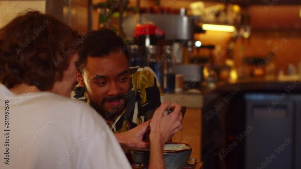 Two people sit at a table in a cafe, they eat and girl shows something on her phone Two people sit at a table in a cafe, they eat and girl shows something on her phone