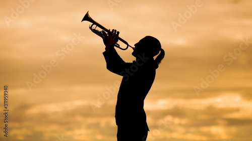 silhouette of a slender trumpeter playing his musical instrument trumpet or horn against background of a yellow sky