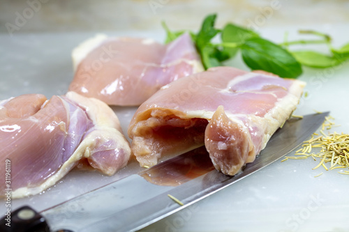 Three skinless chicken thighs on a cutting board with herbs