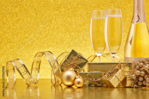 Golden Christmas ornaments, gift boxes, champagne bottle, champagne flutes on festive gold background. Christmas and New Year