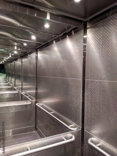 Infinite mirrors in an elevator with lights and metal walls.
