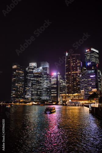 Singapore skyline and river at night with a boat.