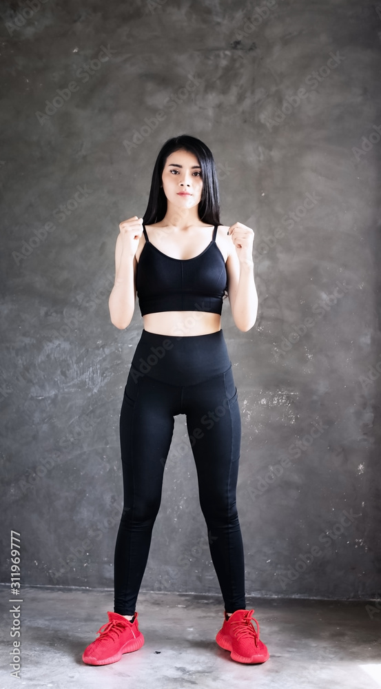 Fototapeta premium The beautiful woman wearing black exercise suit ,raise fists beside her body,doing exercise at home