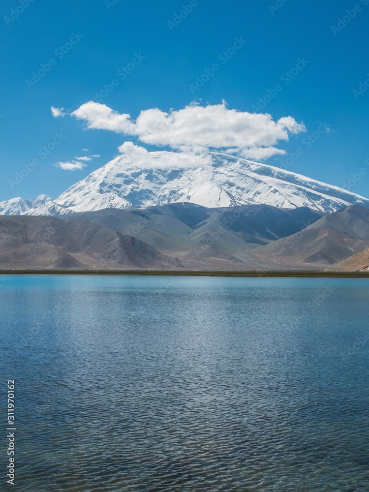 Great cloud covered and snow-capped mountain peak with blue lake water Great cloud covered and snow-capped mountain peak with blue lake water