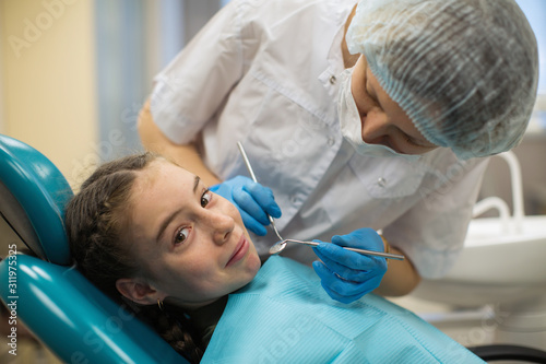 Dentist woman doing teeth checkup of little girl looking with fear in a dental chair in medical clinic.