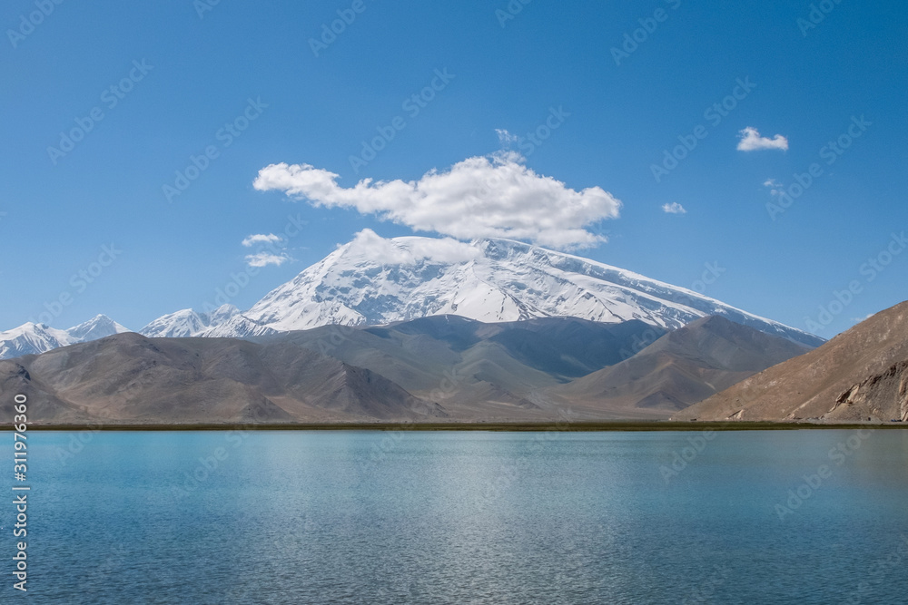 Great cloud covered and snow-capped mountain peak with blue lake water