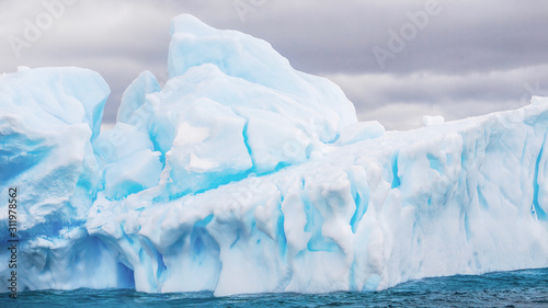 Close-up view of a large iceberg floating in the Weddell Sea in Antarctica, showing details in its blue ice, and deep cracks in its structure.