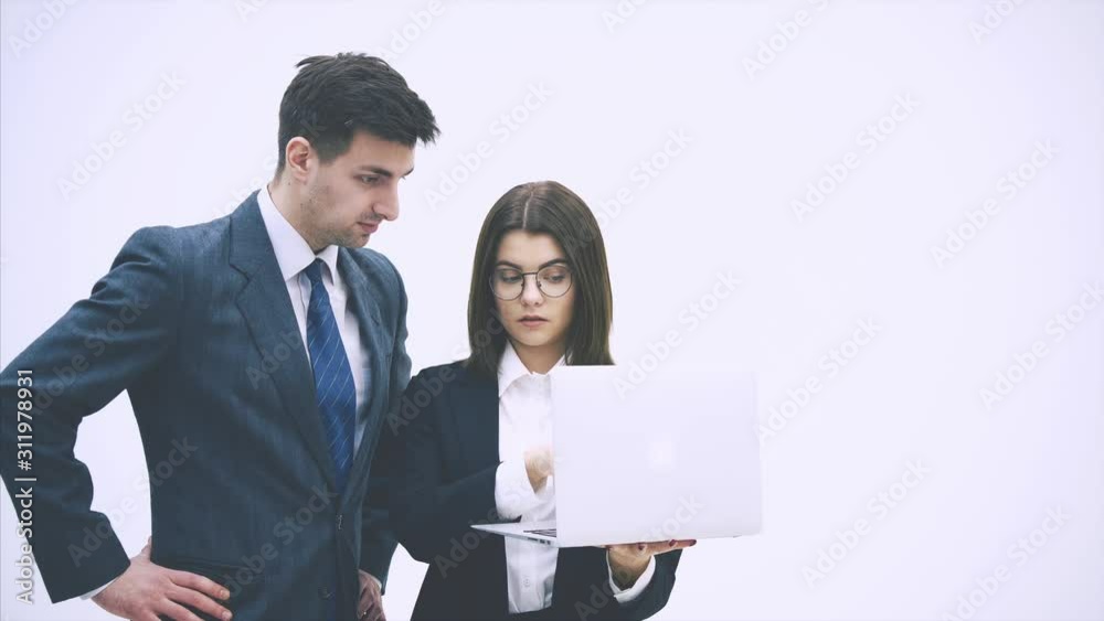 Young business couple standing, looking at something in the laptop, discussing important questions, thinking. Young business couple standing, looking at something in the laptop, discussing important questions, thinking.