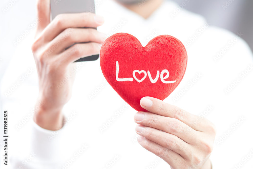 Hand holding red heart with love word and using smartphone Hand holding red heart with love word and using smartphone